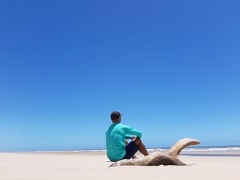 Rear view of man on beach against clear blue sky