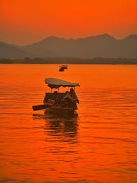 Silhouette person in boat on lake against sky during sunset