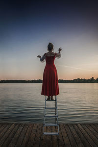 Rear view of woman standing on pier against sky during sunset