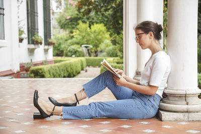 Side view of young woman reading book sitting outdoors