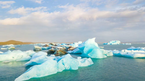 Icebergs in sea against cloudy sky