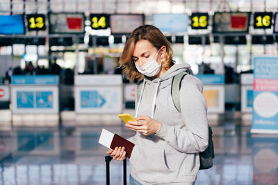 Midsection of woman holding smart phone while standing on laptop