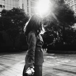 Side view of girl standing by tree against sky