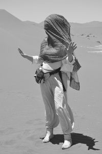 Full length of woman covering face with scarf while standing at desert