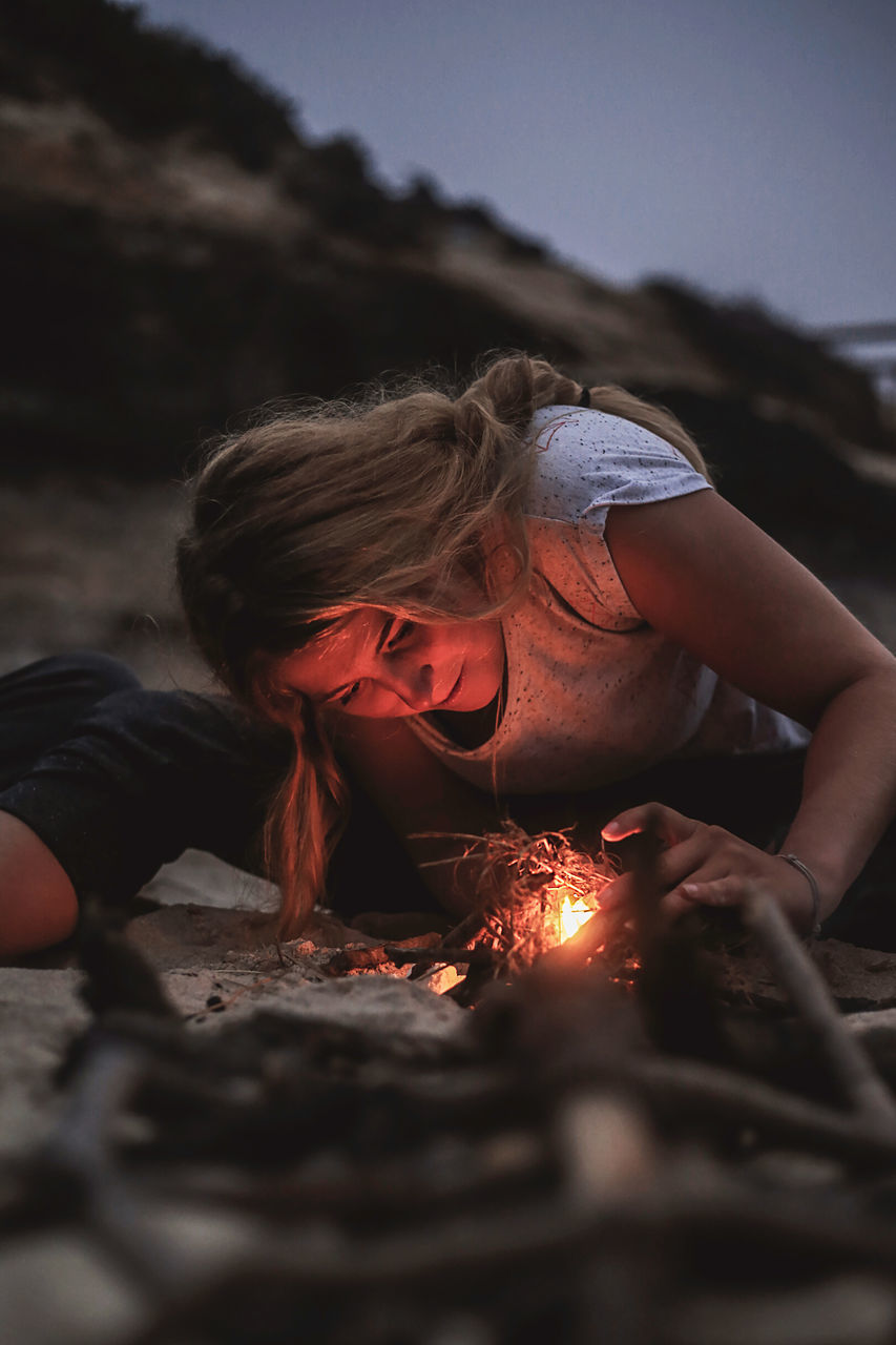 one person, real people, fire - natural phenomenon, fire, burning, leisure activity, selective focus, land, heat - temperature, flame, lifestyles, sky, nature, women, bonfire, beach, young women, casual clothing, hair, outdoors, wood, campfire, hairstyle