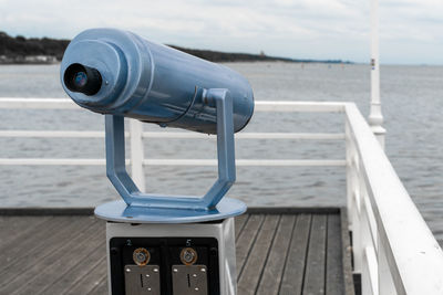 Close-up of coin-operated binoculars by sea against sky