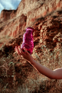 Cropped hand of person holding container against rock formation