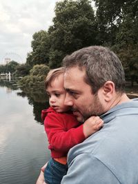 Father carrying baby while looking at lake