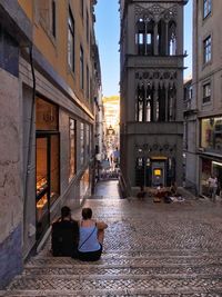 Rear view of people sitting on street amidst buildings in city