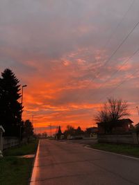 Road by trees against sky during sunset