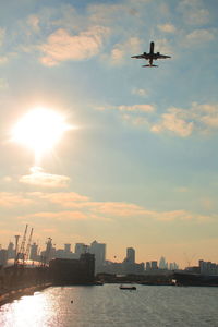 Airplane flying over cityscape against sky during sunset