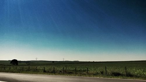 Road by field against clear blue sky