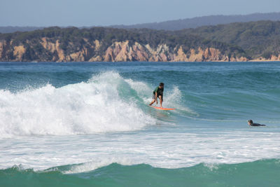 Man surfing on wave in sea against sky