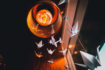 Perspective view from underneath of origami swans hanging from the roof with an old light bulb