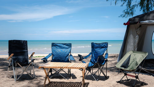 Empty chairs and tables and lounge chair at beach against sky