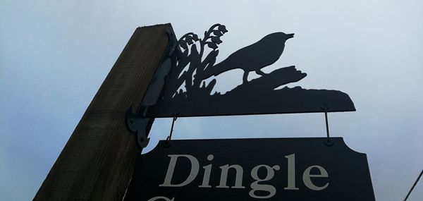 Low angle view of bird perching on a sign