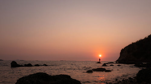 Silhouette fishing man standing on the rock inn the sea and the sunlight background at twilight 