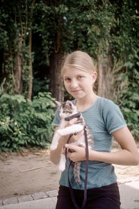 Portrait of woman carrying kitten while standing against trees