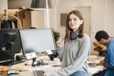 Portrait of smiling female computer programmer using laptop at desk in office