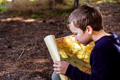 Boy holding paper while sitting in forest