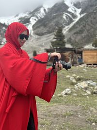 Portrait of young muslim woman wearing sunglasses, hijab or scarf holding camera at the mountain 