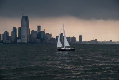 Sailboat sailing on sea by buildings against sky in city