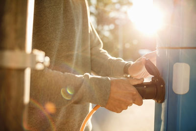 Midsection of man plugging at electric station on sunny day