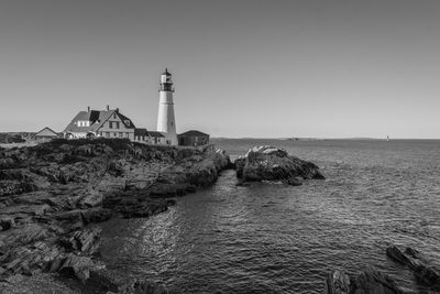 Lighthouse by sea against clear sky