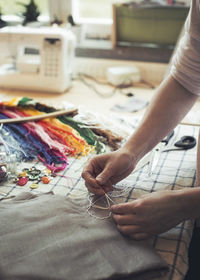 Cropped image of woman stitching fabric on table at home