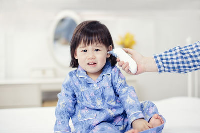 Cropped hand of parent checking temperature of daughter on bed