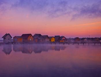 Houses by lake against sky during sunset