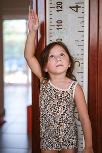 Portrait of a girl standing against wall measuring her height