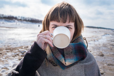 Close-up portrait of young woman drinking coffee at beach