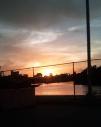 Silhouette bridge over river against sky during sunset