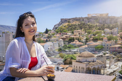 Portrait of smiling young woman in city against sky