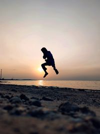 Silhouette man jumping on beach against sky during sunset