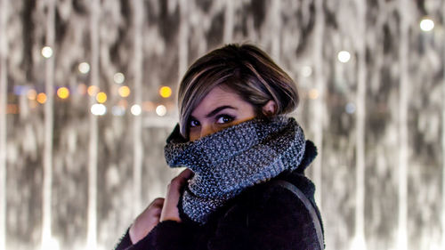 Side view portrait of woman in warm clothing against fountain at night