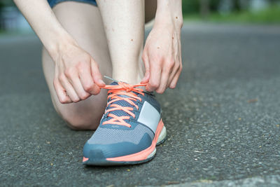 Low section of woman tying shoelace while kneeling on road