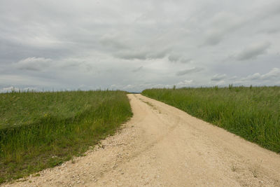 Road passing through field against cloudy sky