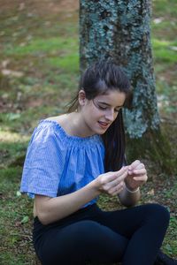 Young woman using mobile phone while sitting on tree