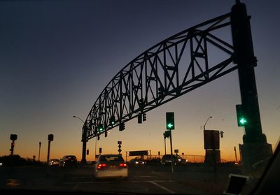 Illuminated stoplight over road against sky during sunset