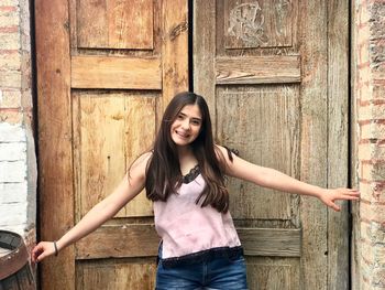 Portrait of smiling young woman standing against closed door