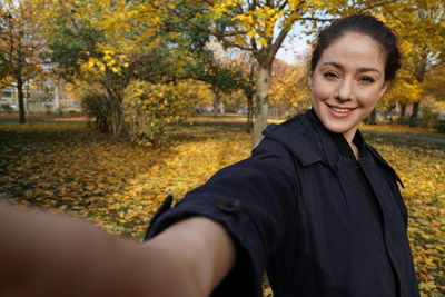 Portrait of smiling young woman standing by trees during autumn