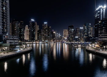 Illuminated buildings by river against sky at night