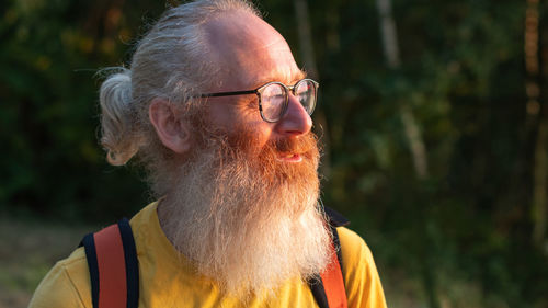 A bearded middle-aged man with glasses in a yellow t-shirt looks at the sunset behind the forest