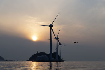 Silhouette of wind turbines in sea against sunset sky