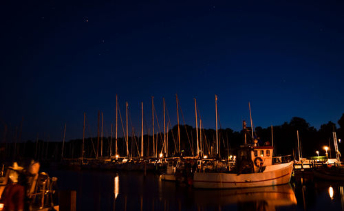 Boats moored at harbor against clear sky at night
