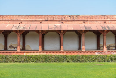 A column-lined walkway and a manicured lawn against blue sky at agra fort in agra,, india