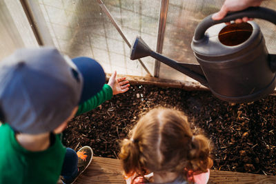 Two young children helping mom water plants in backyard greenhouse