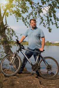 An adult man with a bicycle resting in nature river.